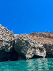 Naklejka premium Sea cave with turquoise crystal water along the rocky Crete coast, Greece. Blue summer sky, bright reflections on water