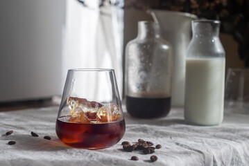 Cold brew coffee in a clear glass with ice on a table covered with a natural linen tablecloth.