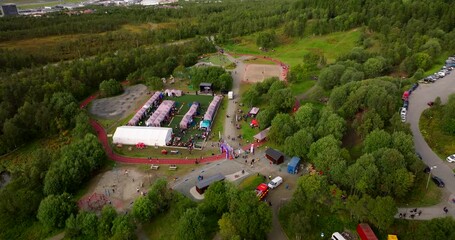 Aerial drone view of the Relay for Life cancer fundraising event in Tromsø, Norway. Participants walk around a track surrounded by tents and green forest during the community gathering