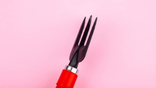 A black gardening tool with a red handle against a soft pink backdrop, close up