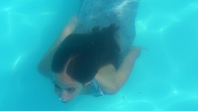 Girl diving underwater during summer swim. Underwater portrait of girl snorkeling. Girl moving underwater in pool. Girl emerging from water on face. Water streaming down her skin as she surfaces.