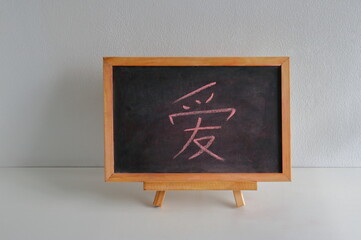 Chinese character means love, is written on chalkboard resting on white wooden table against white...