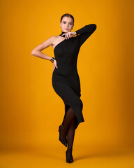 Stylish young woman in a form-fitting black one-shoulder dress posing against a vibrant orange background. Elegant evening fashion.