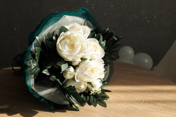 Beautiful white flower bouquet with lush greenery placed on a wooden table in bright light