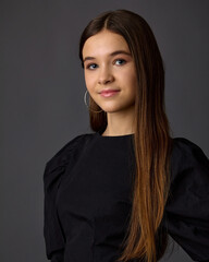 A close-up studio fashion portrait of a young woman wearing a black top with voluminous sleeves and large hoop earrings. Against a dark gray background, the focus is on her beauty and hairstyle.