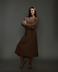 A full-length studio fashion portrait of a young woman wearing a monochrome brown ensemble,...