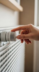 Human hand adjusts the temperature control knob on a white heating radiator indoors
