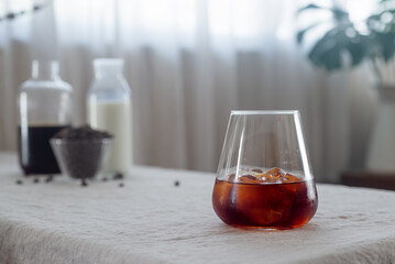 Cold brew coffee in a clear glass with ice on a table covered with a natural linen tablecloth.