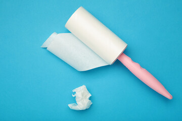 Cloth fabrics cleaner lint roller brush with paper roll on blue background. Sticky roller, pet cat dog fur dust hair remover
