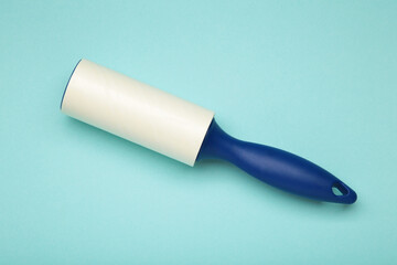 Cloth fabrics cleaner lint roller brush with paper roll on blue background. Sticky roller, pet cat dog fur dust hair remover