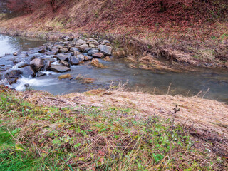 Small natural river with an artificial stone barrier designed to slow water flow, retain water in the landscape, support fish habitat and improve local ecology.