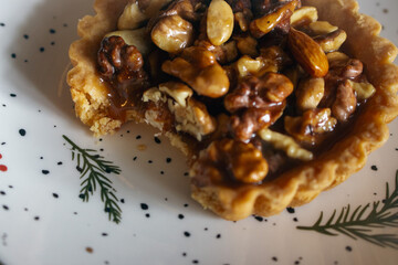 Traditional Christmas tart with nuts and salted caramel on decorated plate. Bitten tart on festive Christmas plate. Bitten hazelnut cake close up. Cinnamon cookie with caramel. Winter holiday food