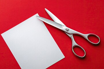 A pair of shiny scissors cutting white paper against a vibrant red background