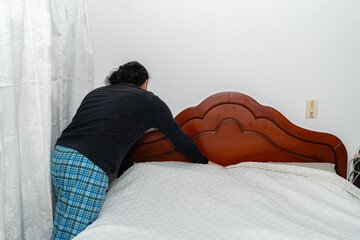 Person adjusting white bedspread from behind in bedroom.