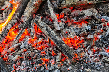 Glowing embers and ashes from a recent campfire surrounded by charred wood and a soft glow at twilight in a tranquil outdoor setting
