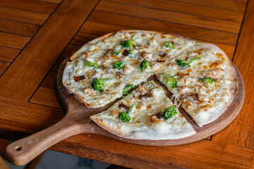 Fresh chicken and broccoli pizza served on a wooden board with one slice pulled out. Ideal for...