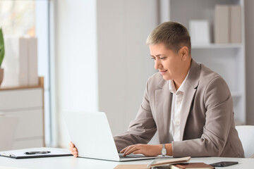 Young businesswoman with short hair and laptop working at desk in office