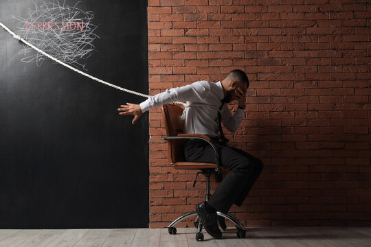 Businessman with rope in chair near word DEPRESSION on black wall. International Stress Awareness Week - Powered by Adobe