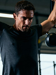 A focused man performs a weightlifting exercise at a gym. He sweats as he works hard, highlighting his dedication to fitness. The modern facility has gym equipment in the background