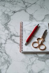 Red Pen And Gold Scissors On White Notebook On Marble Surface