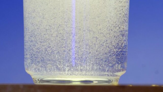 Push-in close-up focusing on rising bubbles in clear sparkling water inside glass