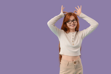 Teenage redhead girl showing OK gestures on lilac background