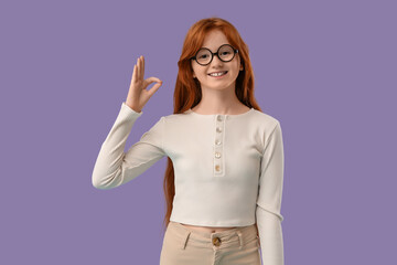 Teenage redhead girl showing OK gesture on lilac background