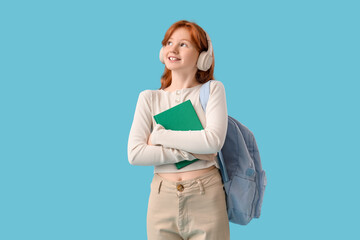 Teenage redhead girl with notebook and backpack on blue background