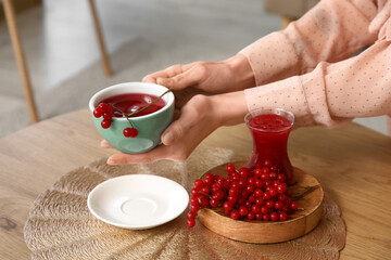 Young woman holding cup of healthy viburnum tea in living room, closeup