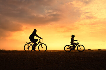 Fototapeta premium Silhouette of Woman and Child Biking in Nature at Sunset – Summer Adventure