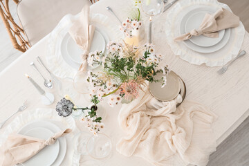 Beautiful table setting with bouquet of flowers and candles in light dining room, top view
