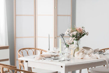Beautiful table setting with bouquet of flowers and candles in light dining room