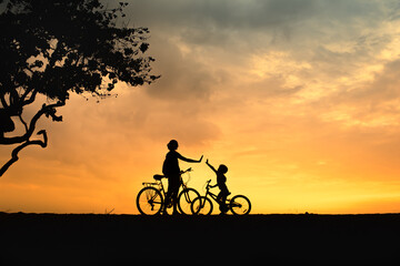 Fototapeta premium Mother and child biking at sunset – silhouette of family high-fiving outdoors, active lifestyle parenting