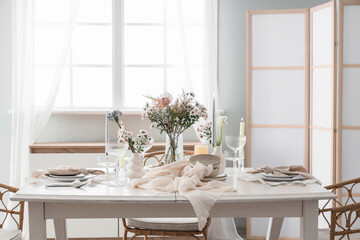 Beautiful table setting with bouquet of flowers and candles in light dining room