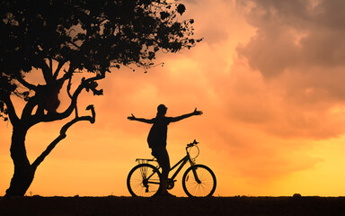 Silhouette of a person cycling at sunset with open arms under tree, freedom and outdoor lifestyle