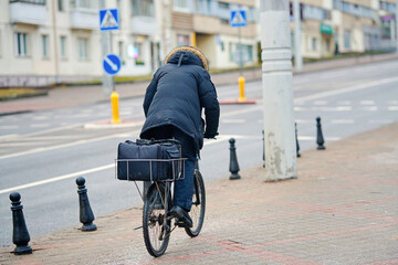 Food delivery, pizza courier on bicycle transports orders through wintry city sidewalk, carrying...