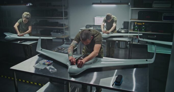 Woman and Men Assembling Advanced Military Drones in Factory. Woman Engineer Works Alongside Male Colleagues, Assembling Advanced Military Drones in Modern Factory Setting. Defense Manufacturing.