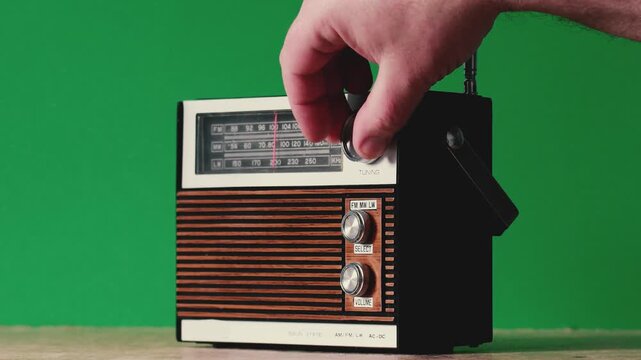 person interacts with an old radio at home, adjusting the antenna and turning the knobs to find different stations. green background.