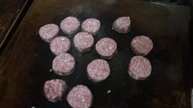 Slices of black pudding grilling on a hot plate