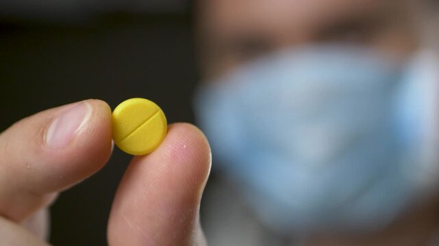 Healthcare expert in mask holding yellow pill, symbol of reliable treatment. Scientific medicine ensuring effective recovery. Modern healthcare approach emphasizing patient well-being
