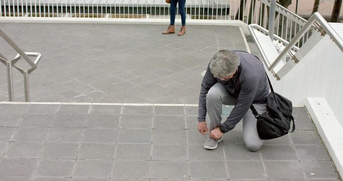 Diverse friends noticing friend kneeling and tying loose sneaker lace on tiled terrace, copy space