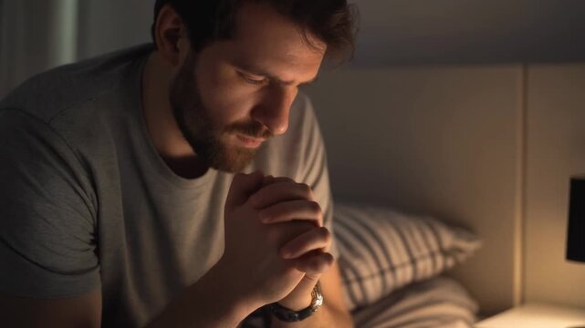 Solemn man with beard praying in his bed at night showing deep faith and spiritual devotion during a quiet moment of reflection and worship before sleep