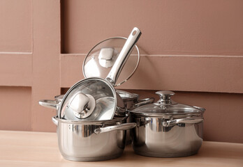 Stainless cooking pots on table near brown wall