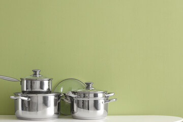 Stainless cooking pots on table near green wall
