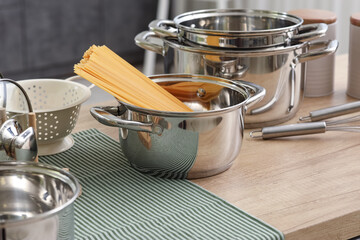 Stainless cooking pots with pasta and utensils on wooden table in kitchen