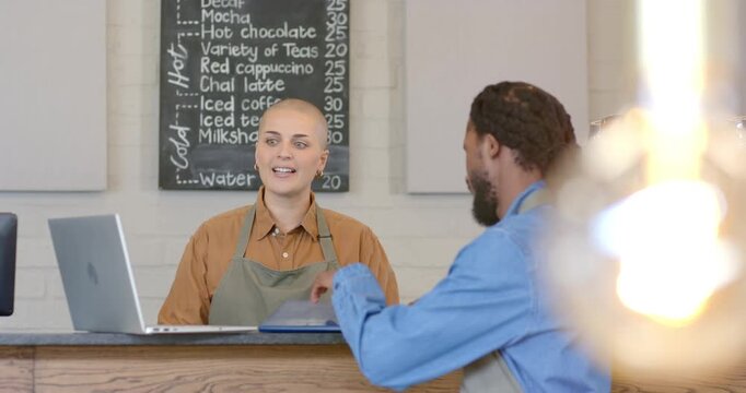 Diverse coworkers at cafe counter exchanging tablet and guiding order training on tablet and laptop