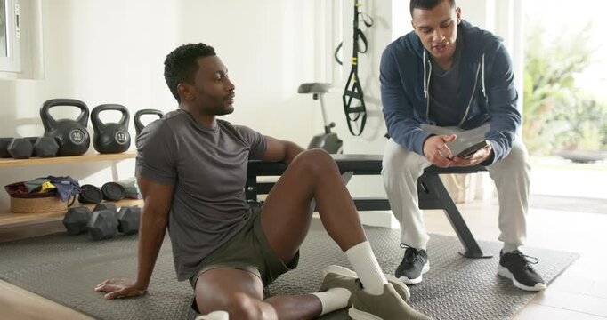 African American trainer pulling smartphone swiping app at gym while guiding client exercise