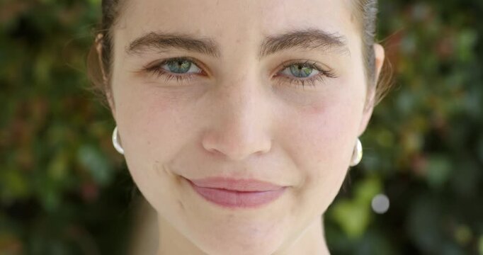 Adult woman raising eyebrows widening eyes smiling wearing silver hoops in yard keeping eye contact