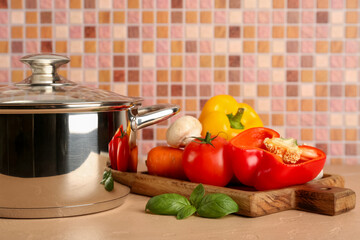 Cooking pot with different vegetables on beige table against pink tile wall