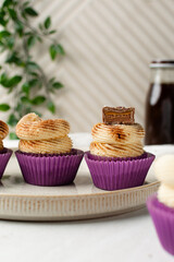 Close-up of a vanilla cupcake in a pink wrapper with buttercream frosting, cinnamon dust, and a caramel-filled chocolate, cupcake in a pink liner with a cinnamon frosting and caramel chocolate bar